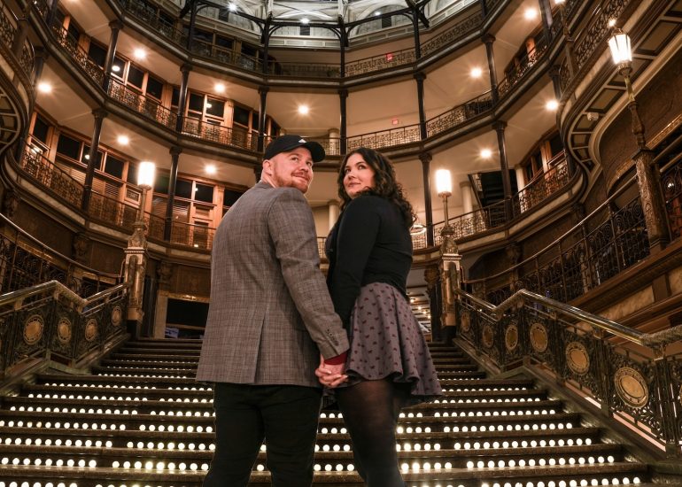 Engagement proposal couple holding hands on the grand Arcade staircase during their Cleveland portraits.