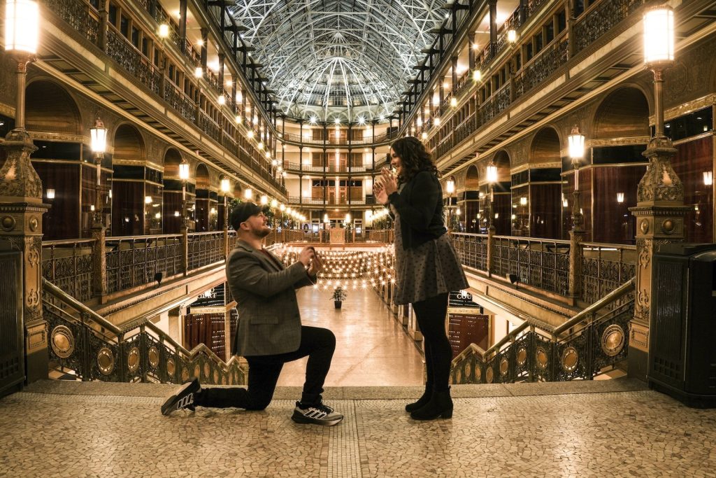 One partner in Ohio kneels to during proposal beneath the glass roof of the Cleveland Arcade.