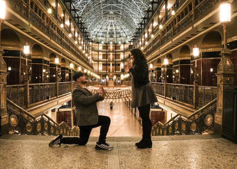One partner in Ohio kneels to during proposal beneath the glass roof of the Cleveland Arcade.